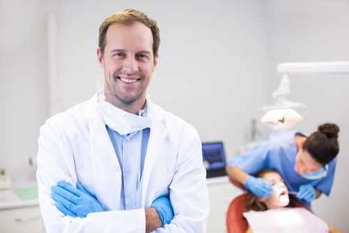 רופא שיניים עומד מחוייך עם ידיים שלובות