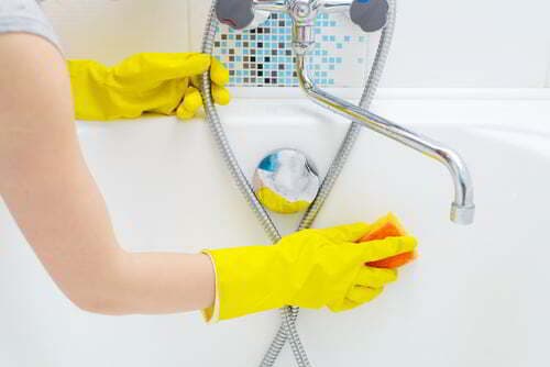 אישה מנקה אמבטיה עם כפפות גומי וסקוץ